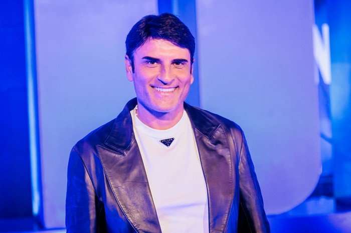 Sal Da Vinci smiling ahead wearing a white t-shirt and brown leather jacket.