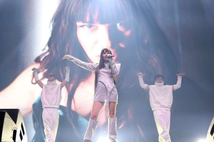 ESSYLA performing on stage singing into a microphone with her other arm outstretched.