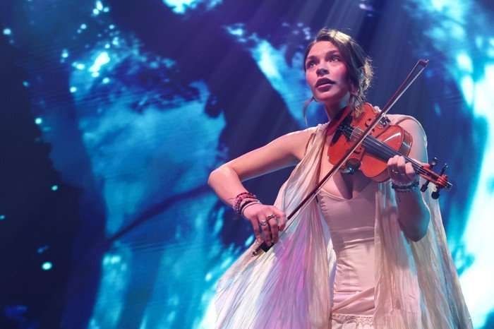 Eva Marija stood on stage playing violin, slightly hunched over as she looks into the crowd.