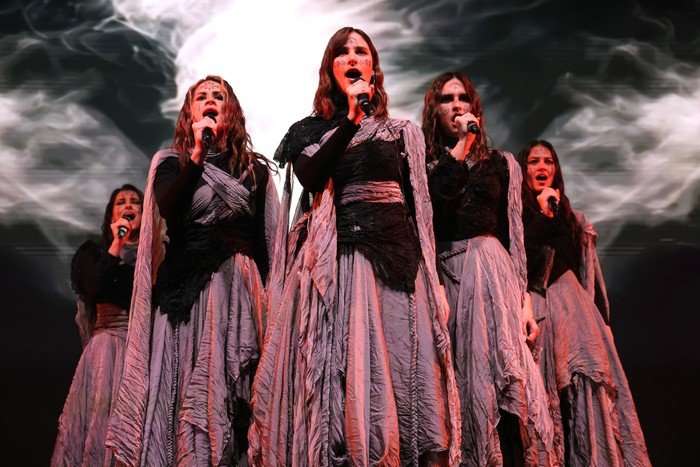 The members of LELEK standing as a group on stage and singing into microphones.