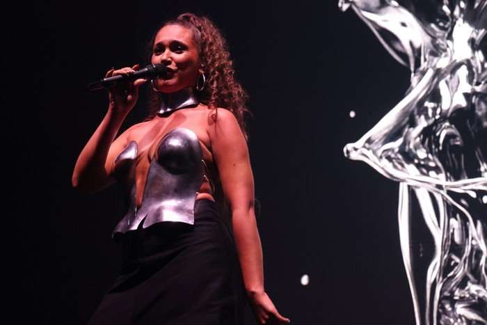 Alicja stood on stage holding a microphone, wearing a silver corset and black skirt.