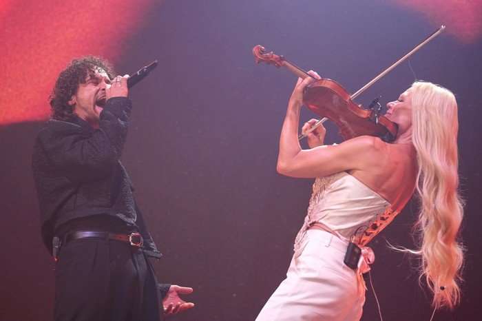Pete Parkkonen and Linda Lampenius facing each onstage whilst Pete sings into a microphone and Linda plays the violin.