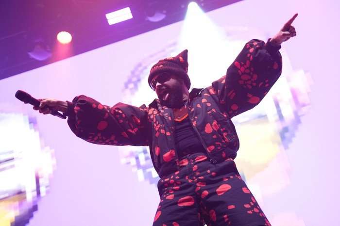 Akylas stood on stage with his arms extended and a microphone in one hand.