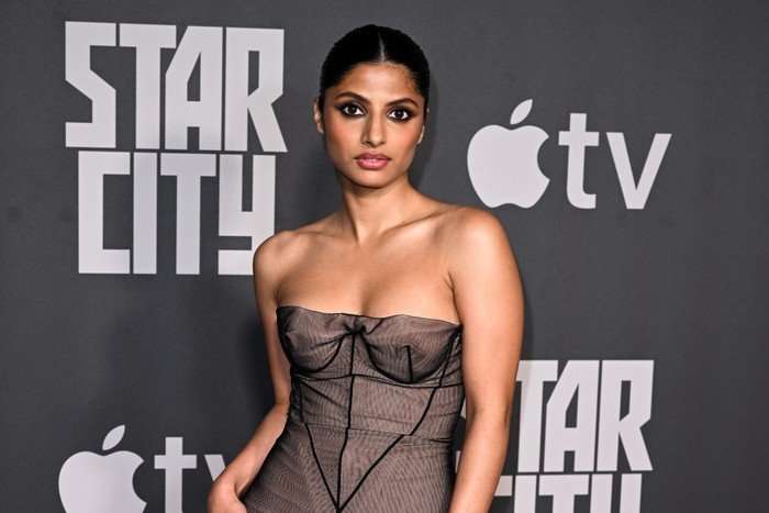 Priya Kansara, wearing a brown dress, stood in front of a black backdrop.
