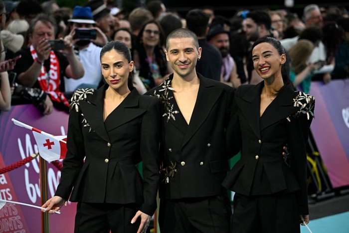 AUSTRIA-ENTERTAINMENT-MUSIC-TELEVISION-ESC Three people wearing match black suits smiling ahead as they pose for a photo.