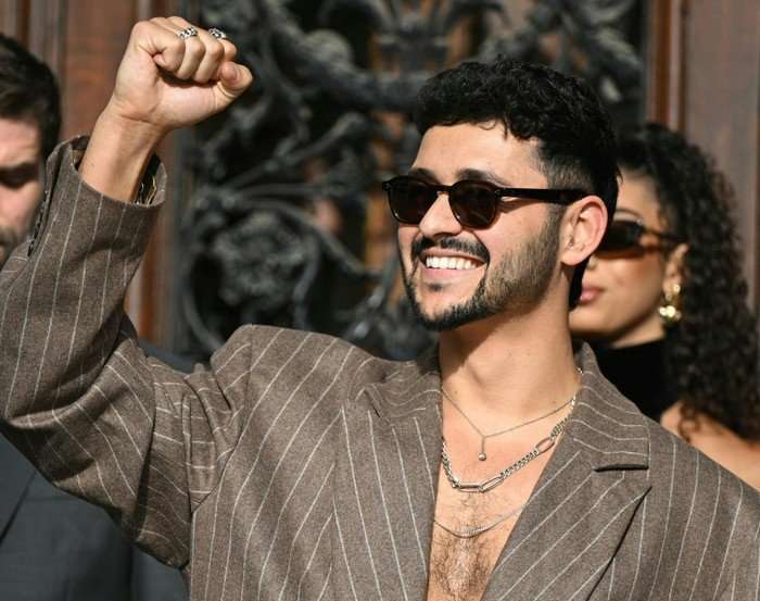 AUSTRIA-ENTERTAINMENT-MUSIC-TELEVISION-ESC Noam Bettan wearing an all brown suit, smiling ahead while holding his fist in the air.