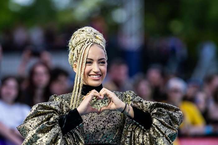 Monroe smiling ahead making a heart symbol with her hands.