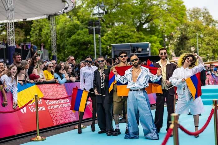 Sim&oacute;n wearing a silk blue outfit holding the Armenia flag, with a group of people stood around him.