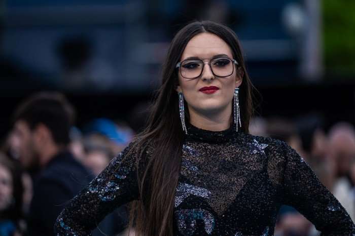 A close up of Veronica Fusaro wearing a black dress and red lipstick looking ahead.