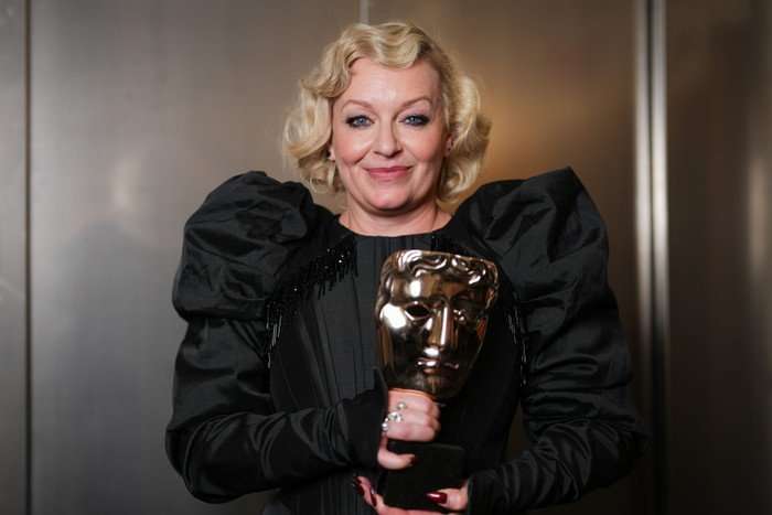 Christine Tremarco holding her BAFTA Award and smiling ahead.
