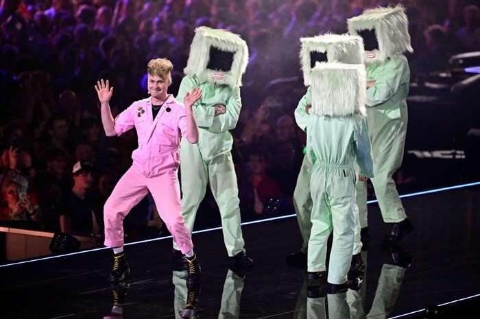 Sam Battle, aka Look Mum No Computer wearing a pink boiler suit stood on stage with his hands in he air.