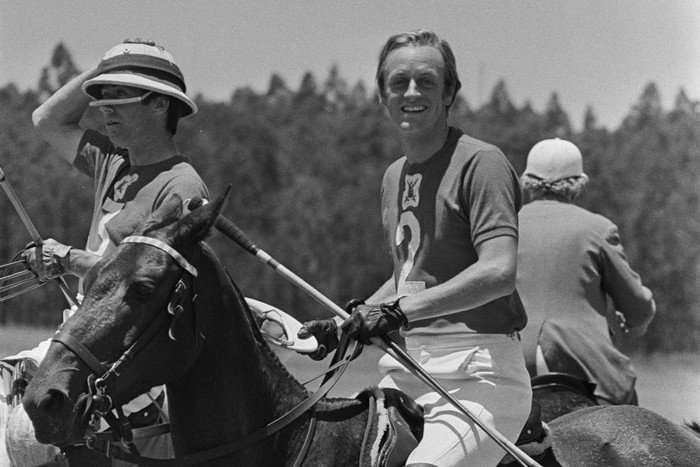 A black and white photo of a young Andrew Parker Bowles playing polo in Kenya