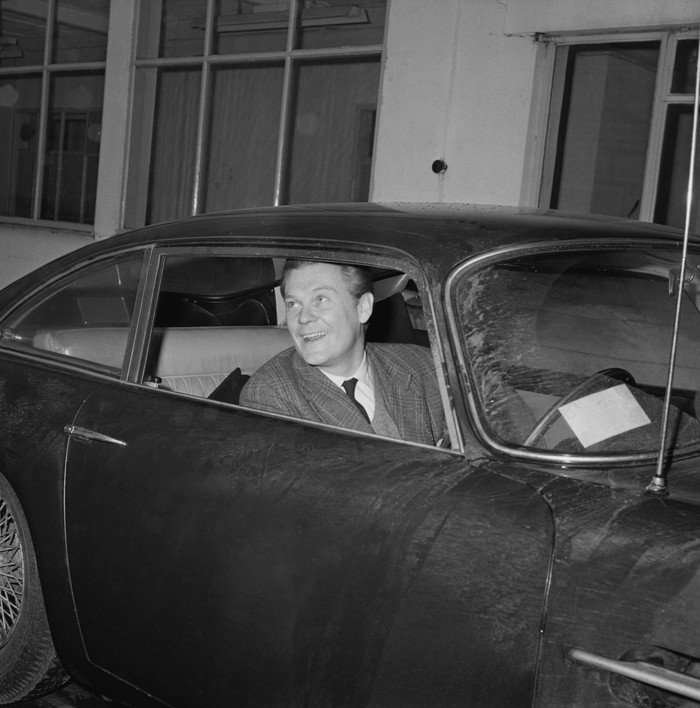 A black and white photo of Michael Howard, the 21st Earl of Suffolk in a car