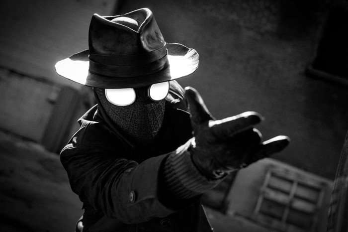 GqyN_DDXcAAEnsP Spider-Man Noir holding his hand out in a classic Spider-Man pose, wearing a trilby hat, trench coat and mask