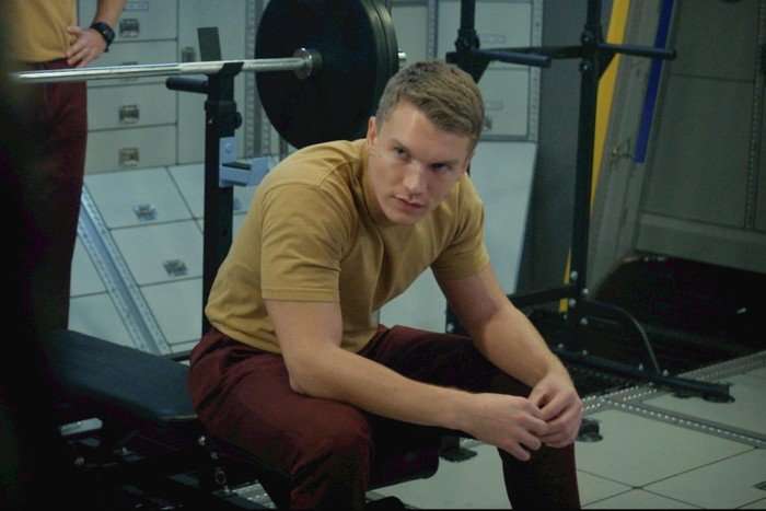 Connor Storrie in For All Mankind season 5 episode 8 Connor Storrie sitting on a bench with his hair cropped short, in a khaki tshirt in For All Mankind season 5 episode 8