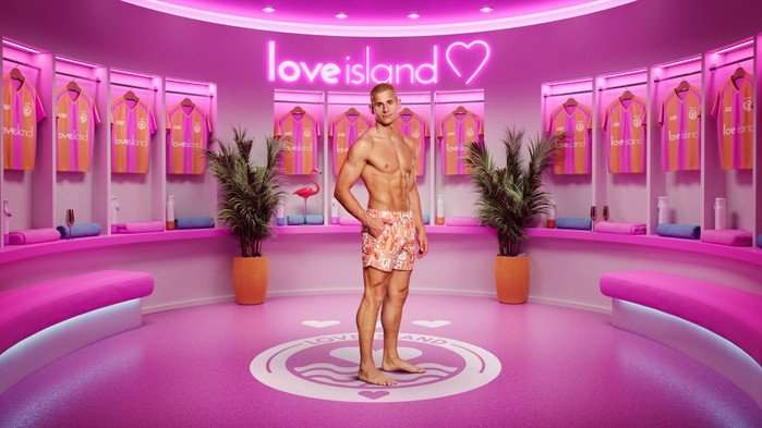 ©ITV A man stood with his body turned to the side wearing floral swim shorts with one hand in his pocket.