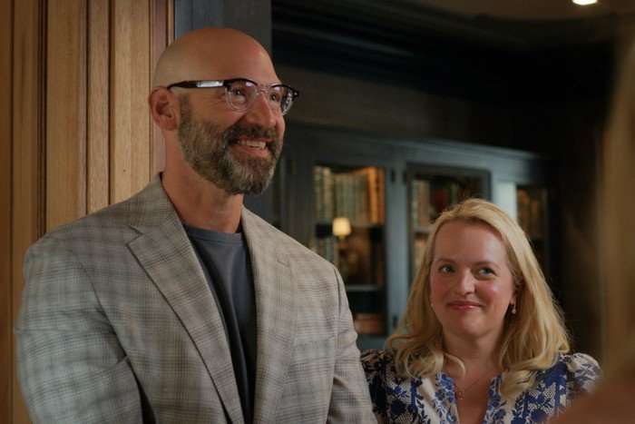 Imperfect_Women_Photo_010403 Corey Stoll and Elisabeth Moss in Imperfect Women, stood next to each other in a room, smiling at someone off screen.