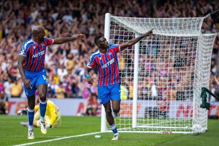 Ismaila Sarr, in blue and red Crystal Palace football kit, points to the crowd as he celebrates alongside a teammate scoring at Selhurst Park.