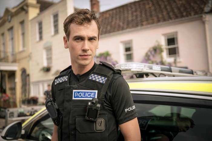 A Good Girl's Guide To Murder Jackson Bews as Dan Da Silva, wearing his police uniform, standing outside