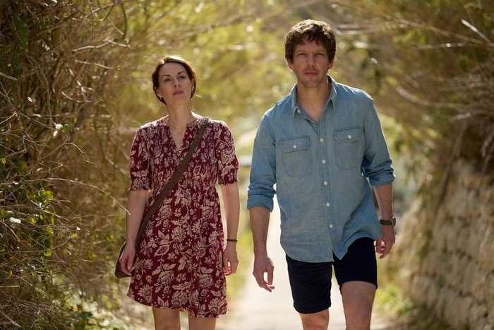 Jessica Raine and Damien Molony star in Two Weeks in August; they are wearing summery clothes and walking down a rural path with trees on both sides