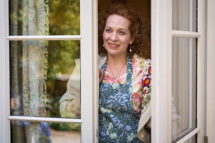 Katherine Parkinson in Rivals season 2 opening up her front door and standing in the doorway, smiling, wearing an apron.