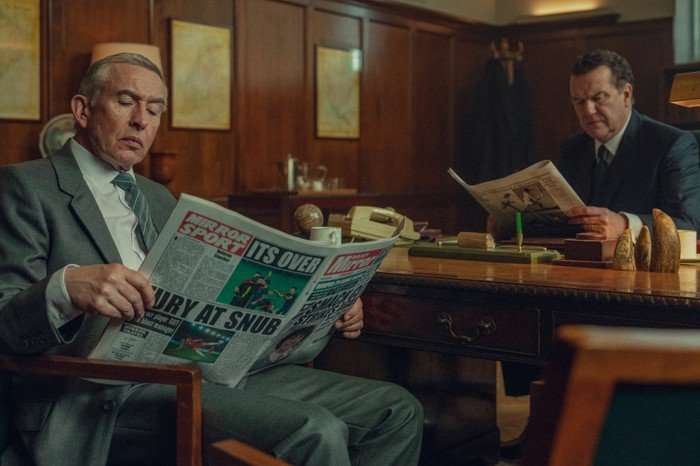 Steve Coogan as Don and Doulgas Hodge as Blake in Legends. They are sat either side of a desk, both wearing suits and reading newspapers.