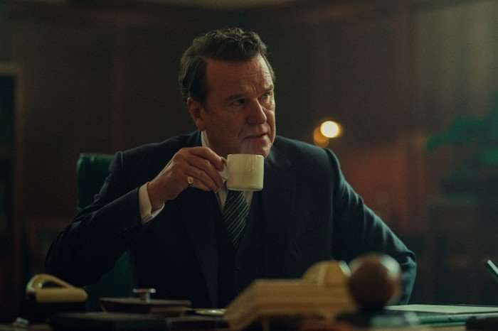 Doulgas Hodge as Blake in Legends, sat at a desk and holding a cup.