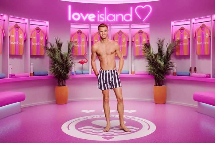 ©ITV Samuel standing in front of a pink Love Island background.