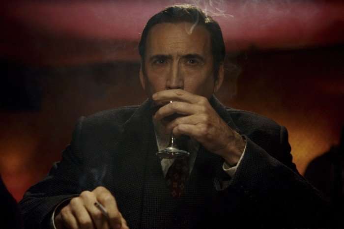 Nicolas Cage as Ben Reilly in Spider-Noir Nicolas Cage as Ben Reilly in Spider-Noir, seated in a shadowy bar, holding a drink and a cigarette as he looks ahead with a wary, world-weary expression.