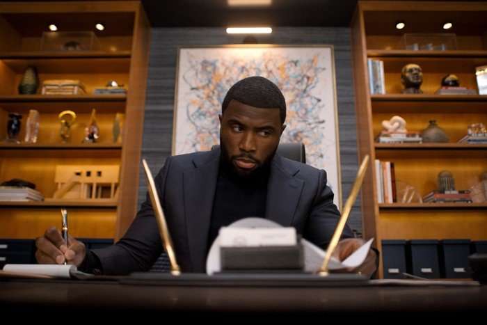 Nemesis_n_S1_E3_00_11_29_10R Y'Lan Noel as Coltrane Wilder in Nemesis, sat at a desk and wearing a black jacket and polo neck.