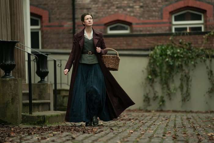 Caitr&iacute;ona Balfe in Outlander season 7 part 2 walking down a cobbled street and holding a wicker basket.