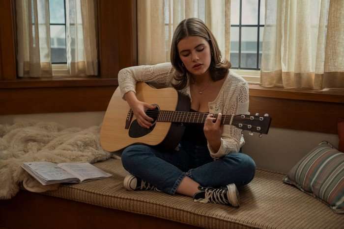 Off Campus Hannah Wells sits cross-legged in her room, playing the guitar by an open window