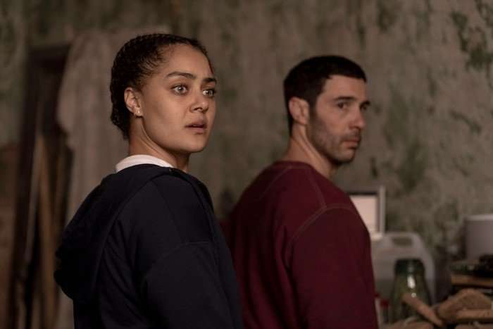 Izuka Hoyle and Tahar Rahim in Prisoner looking surprised as they look to the window, both standing close together.
