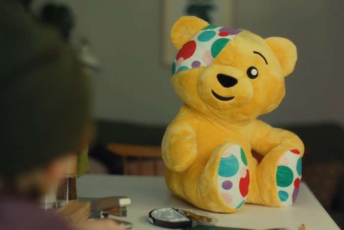 Pudsey sitting on a dining table, facing a child.