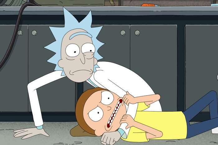 Rick restrains Morty on the floor in a chaotic moment in Rick and Morty season 9, Morty grimacing as Rick leans over him in the lab.