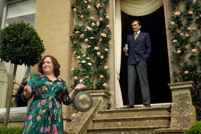 Claire Rushbrook gesturing towards the top of the stairs where David Tennant stands proudly.
