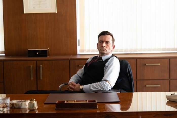 David Tennant as Tony Baddingham in Rivals season 2 sitting at his desk, crossing his arms and looking sternly across the room.