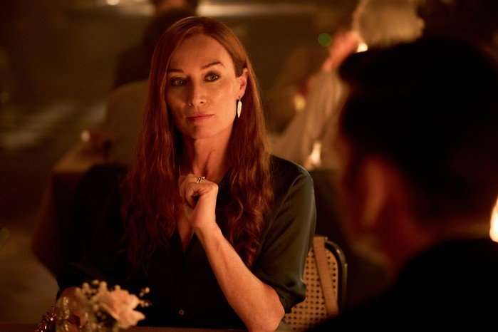 Victoria Smurfit as Maud O'Hara in Rivals season 2 sitting across the table from people in a dimly lit bar, looking nervous.