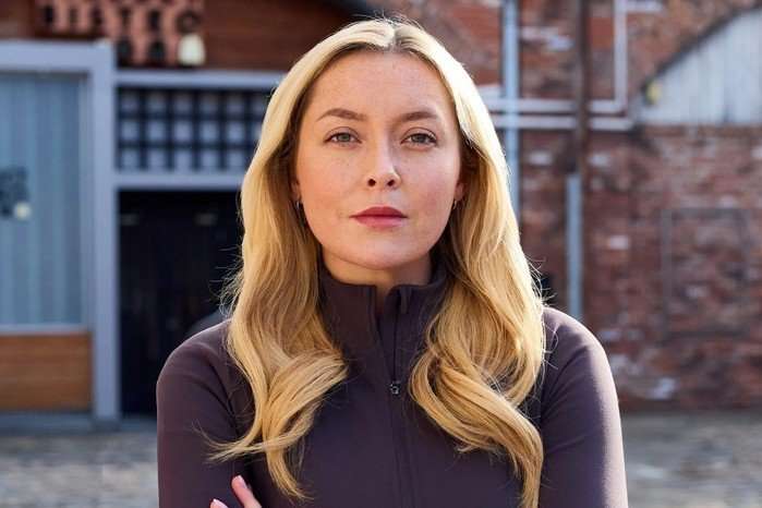 Megan Walsh in a brown dress stood in Coronation Street