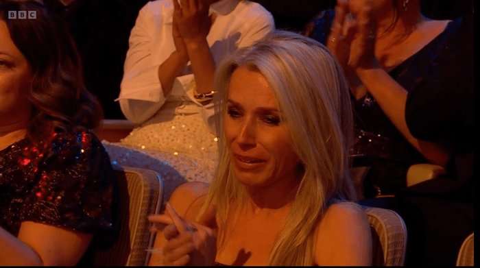 A blonde women in a silver dress weeps in the audience of an awards ceremony