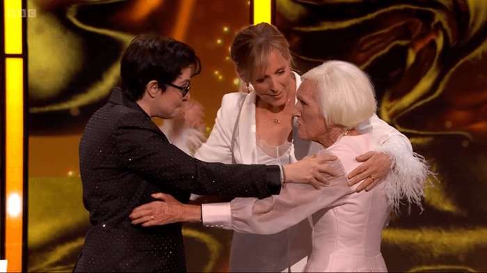 Sue Perkins, in a black suit, Mel Giedroyc in a white sure, and Mary Berry in a pink dress hug on stage
