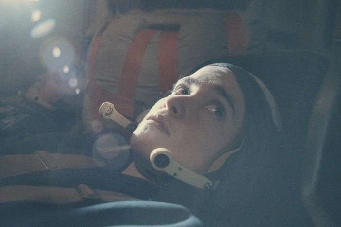 Alice Englert as Anastasia Belikova in Star City. Wearing an astronaut uniform, she stares towards the ceiling.