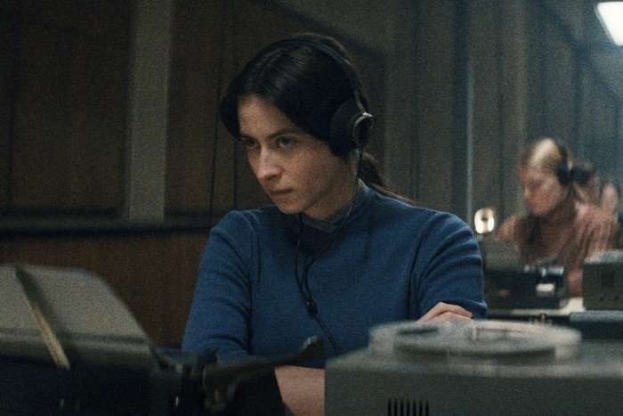 Agnes O'Casey as Irina Morozova in Star City, wearing a blue top and sat at a desk with headphones on.