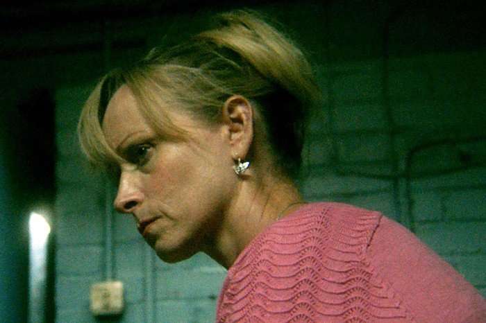 Laura Bayston as Kate McCann in Under Suspicion: Kate McCann. Laura Bayston as Kate McCann in Under Suspicion: Kate McCann, side-on, wearing a pink jumper and sitting in a room with plain white walls.