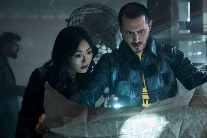 Tomer Capone as Frenchie and Karen Fukuhara as Kimiko in The Boys, pointing a torch at a newspaper and looking at it together.