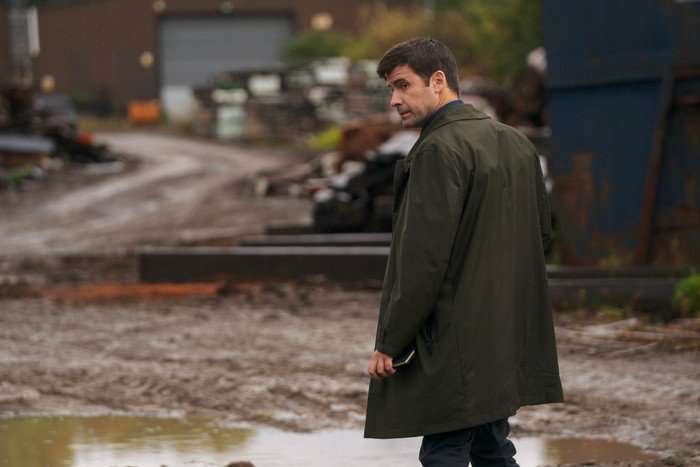 THE_DARK_MarkRowley Mark Rowley as Detective Connor Crawford walking through a wet and muddy plot of land, standing in the centre and looking behind him.
