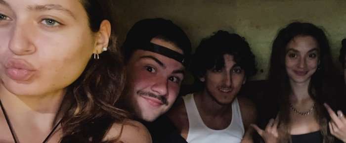 A group of four people all sat down next to each other smiling for a selfie.