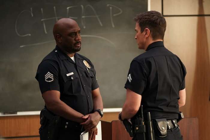 Richard T Jones as Wade Grey and Nathan Fillion as John Nolan in The Rookie having a conversation while standing up in front of a chalkboard, both wearing police uniforms.
