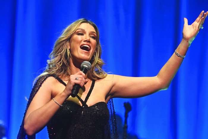 Delta Goodrem singing on stage holding the microphone to her mouth with other arm outstretched.