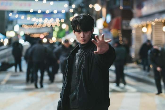 Cha Eun-woo as Lee Un-jeong in The Wonderfools; he is standing on a busy high street, wearing dark-coloured clothing and holding his hand out in a show of his telekinetic powers